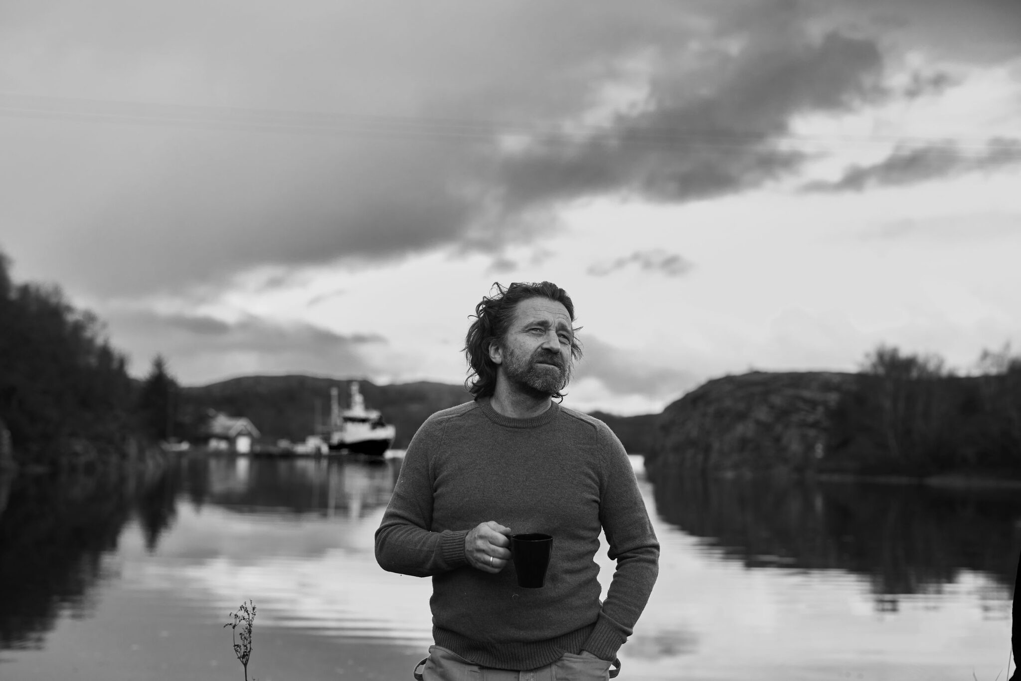 Founder, architect, and cabinet maker Volker Hempelmann by a rocky fjord arm with a fishing boat. nordlys møbler: HANDMADE - SCANDINAVIAN - FURNITURE from Norwegian oak